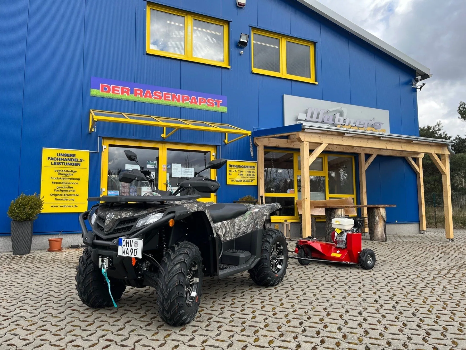 Firmengebäude von Wabner´s Bautechnik am Havelring in Velten, blaue Halle mit gelben Fenstern, davor ein Quad mit Anbau-Schlegelmäher